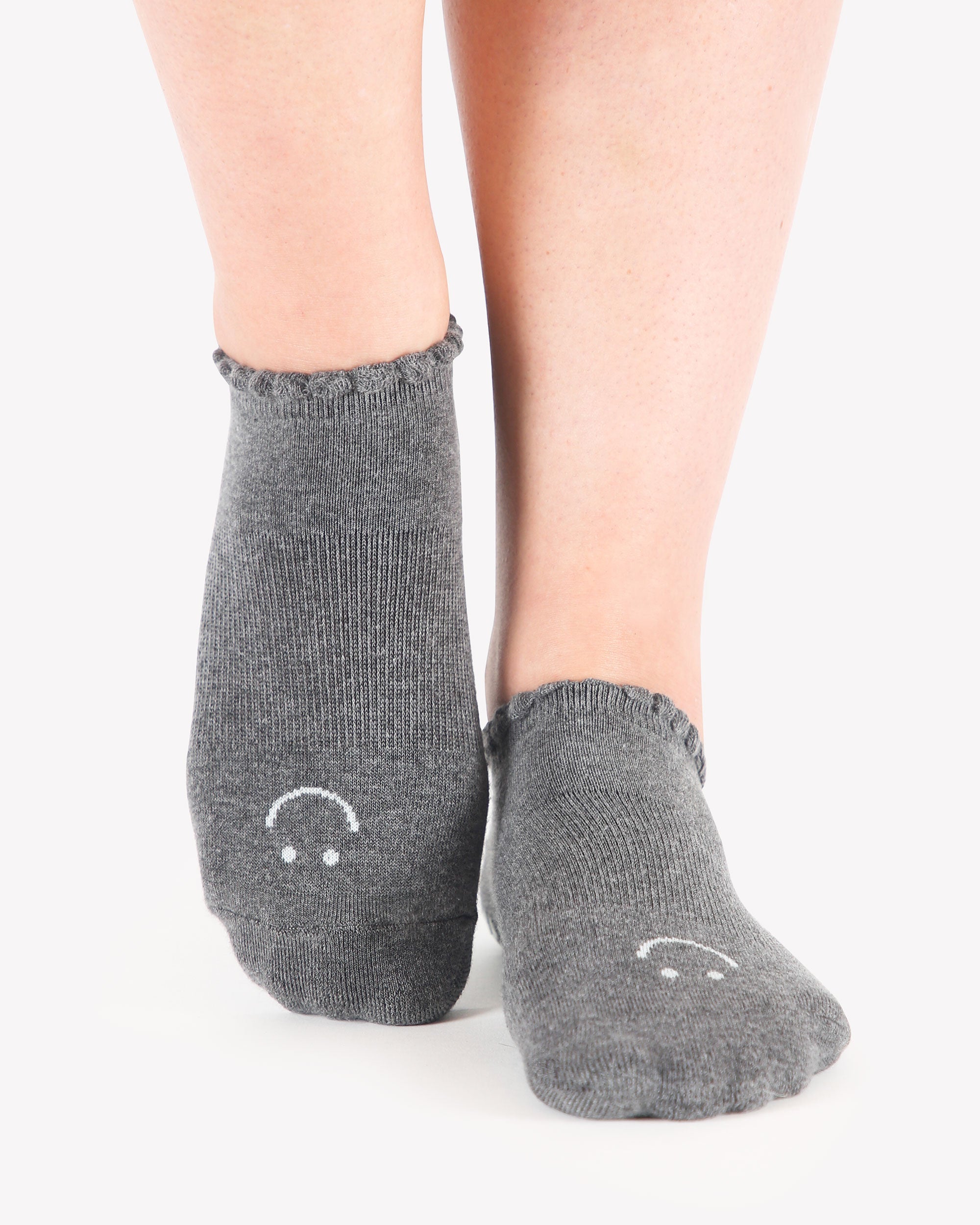 Women wearing gray grip socks with white smiley face for Pilates, Barre, Yoga, and beyond. 