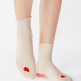 Women wearing a off white ankle grip sock with a red heart motif on the top made for Pilates, Barre, Yoga, and beyond. 