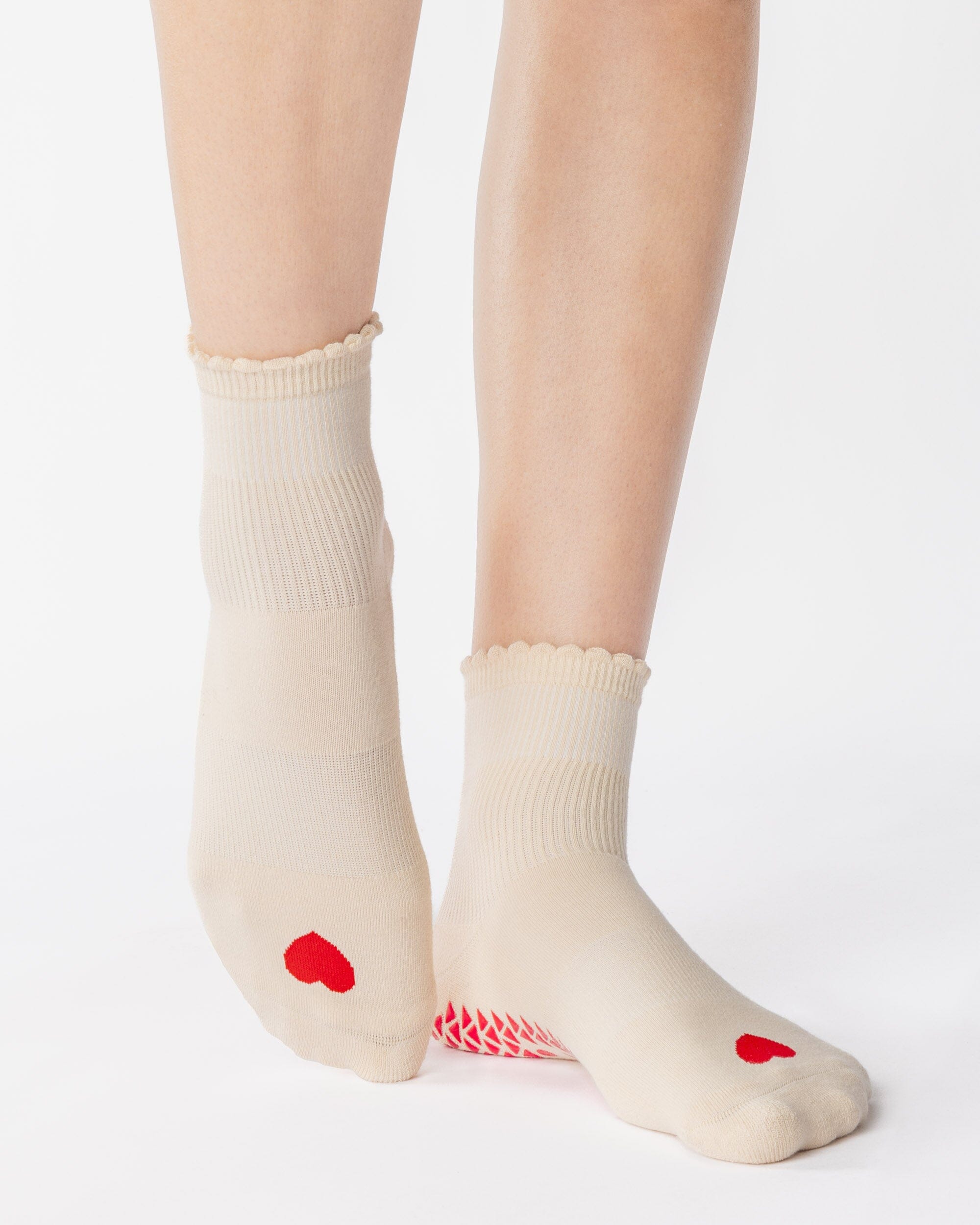 Women wearing a off white ankle grip sock with a red heart motif on the top made for Pilates, Barre, Yoga, and beyond. 