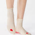 Women wearing a off white ankle grip sock with a red heart motif on the top made for Pilates, Barre, Yoga, and beyond. 