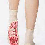 Women wearing a off white ankle grip sock with a red heart motif on the top made for Pilates, Barre, Yoga, and beyond. 