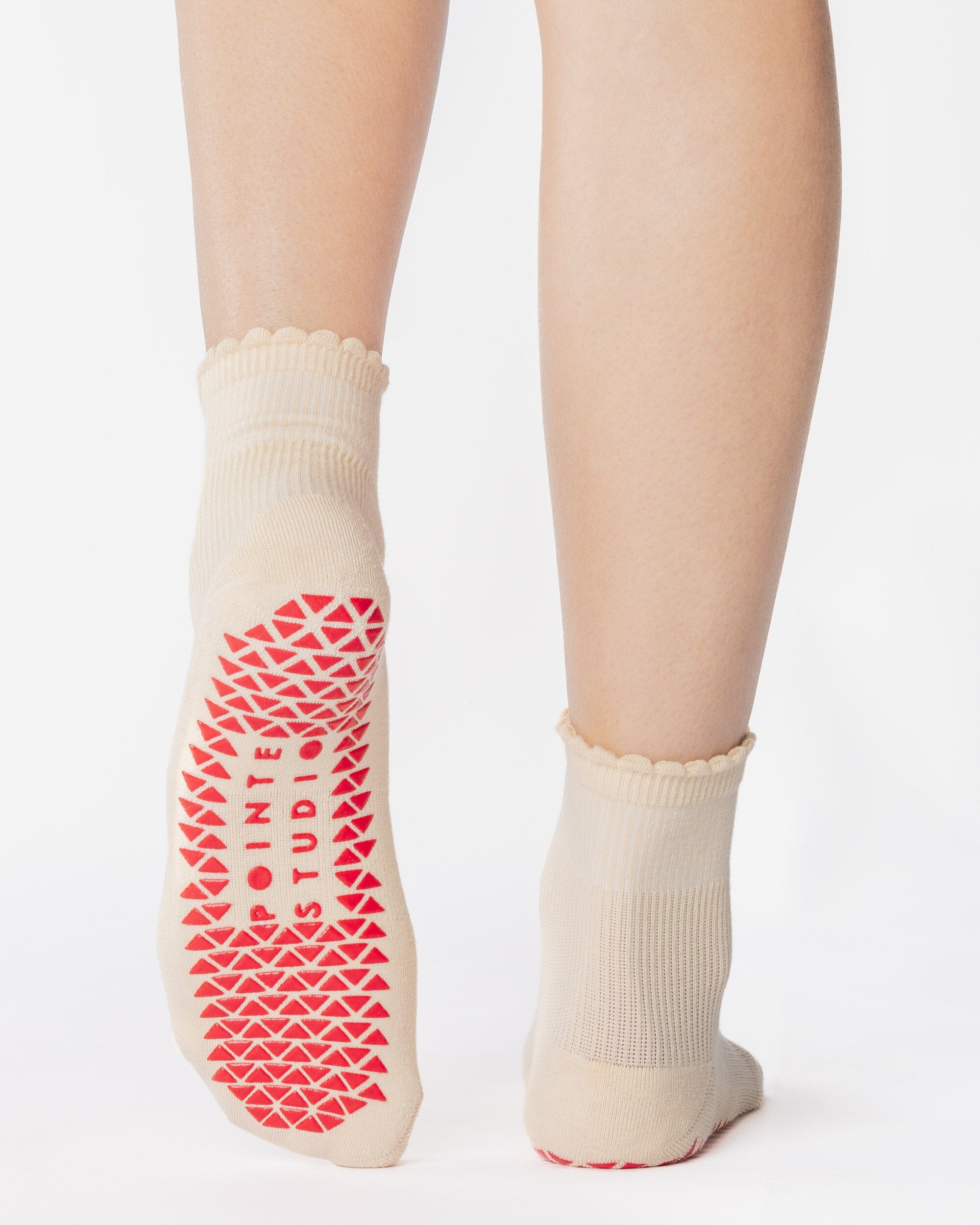Women wearing a off white ankle grip sock with a red heart motif on the top made for Pilates, Barre, Yoga, and beyond. 