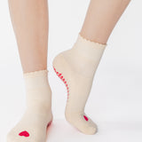 Women wearing a off white ankle grip sock with a red heart motif on the top made for Pilates, Barre, Yoga, and beyond. 