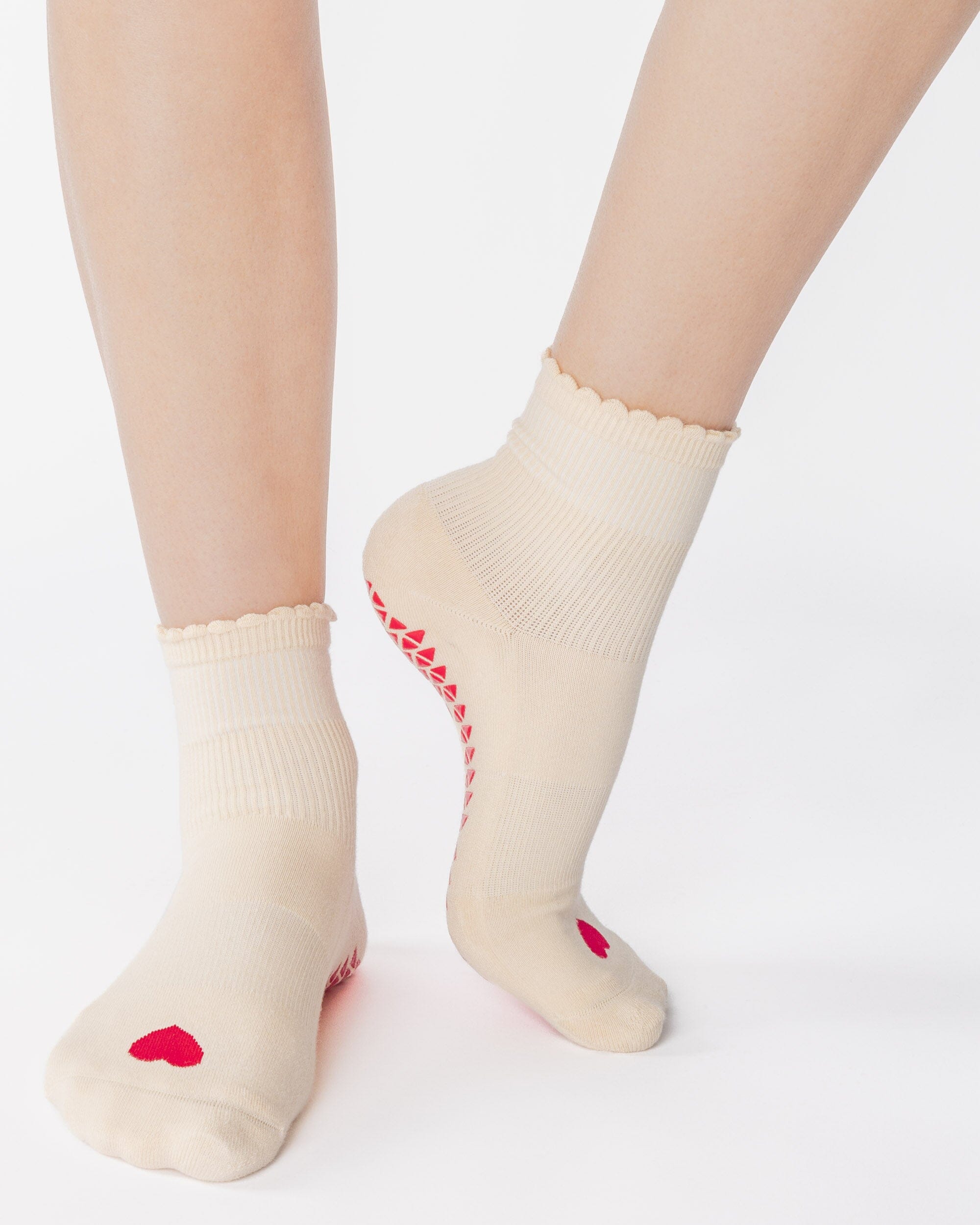 Women wearing a off white ankle grip sock with a red heart motif on the top made for Pilates, Barre, Yoga, and beyond. 