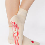 Women wearing a off white ankle grip sock with a red heart motif on the top made for Pilates, Barre, Yoga, and beyond. 