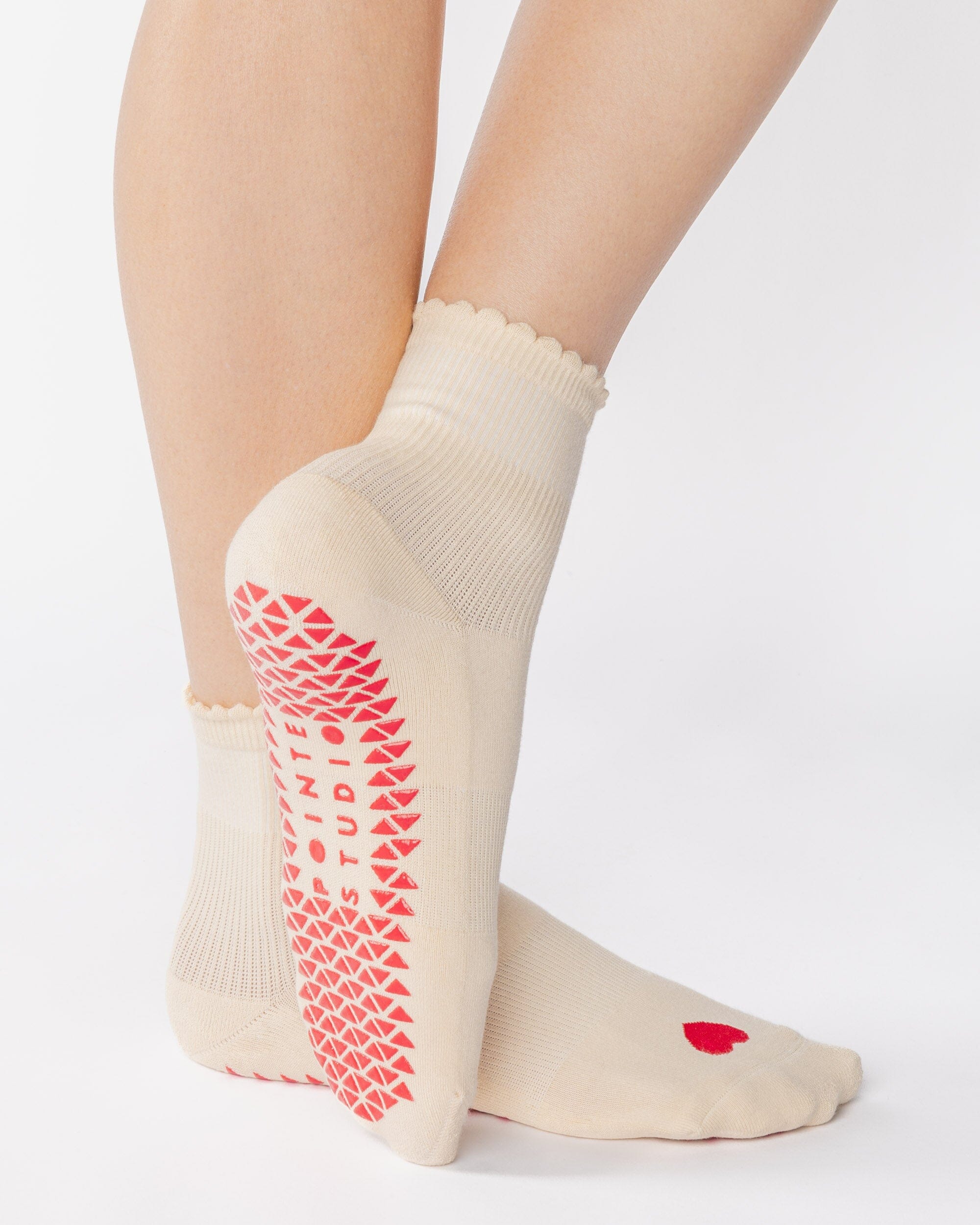 Women wearing a off white ankle grip sock with a red heart motif on the top made for Pilates, Barre, Yoga, and beyond. 