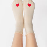 Women wearing a off white ankle grip sock with a red heart motif on the top made for Pilates, Barre, Yoga, and beyond. 