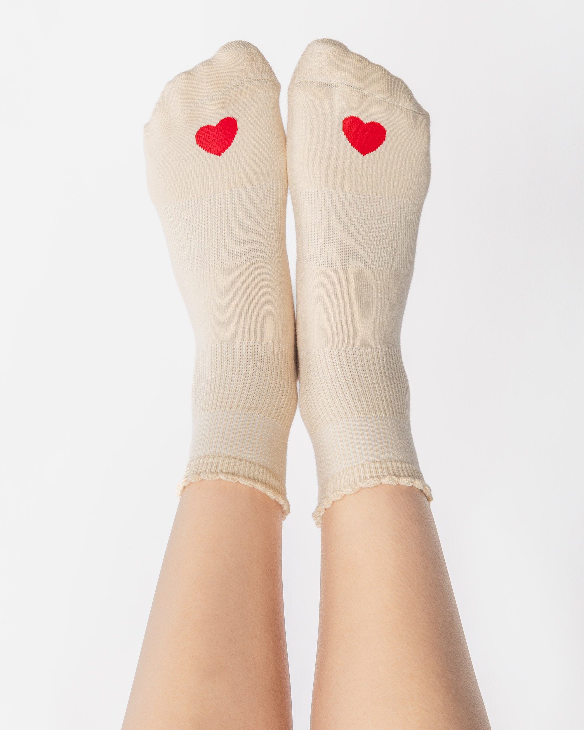 Women wearing a off white ankle grip sock with a red heart motif on the top made for Pilates, Barre, Yoga, and beyond. 