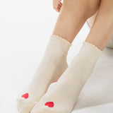 Women wearing a off white ankle grip sock with a red heart motif on the top made for Pilates, Barre, Yoga, and beyond. 