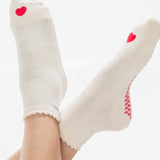 Women wearing a off white ankle grip sock with a red heart motif on the top made for Pilates, Barre, Yoga, and beyond. 