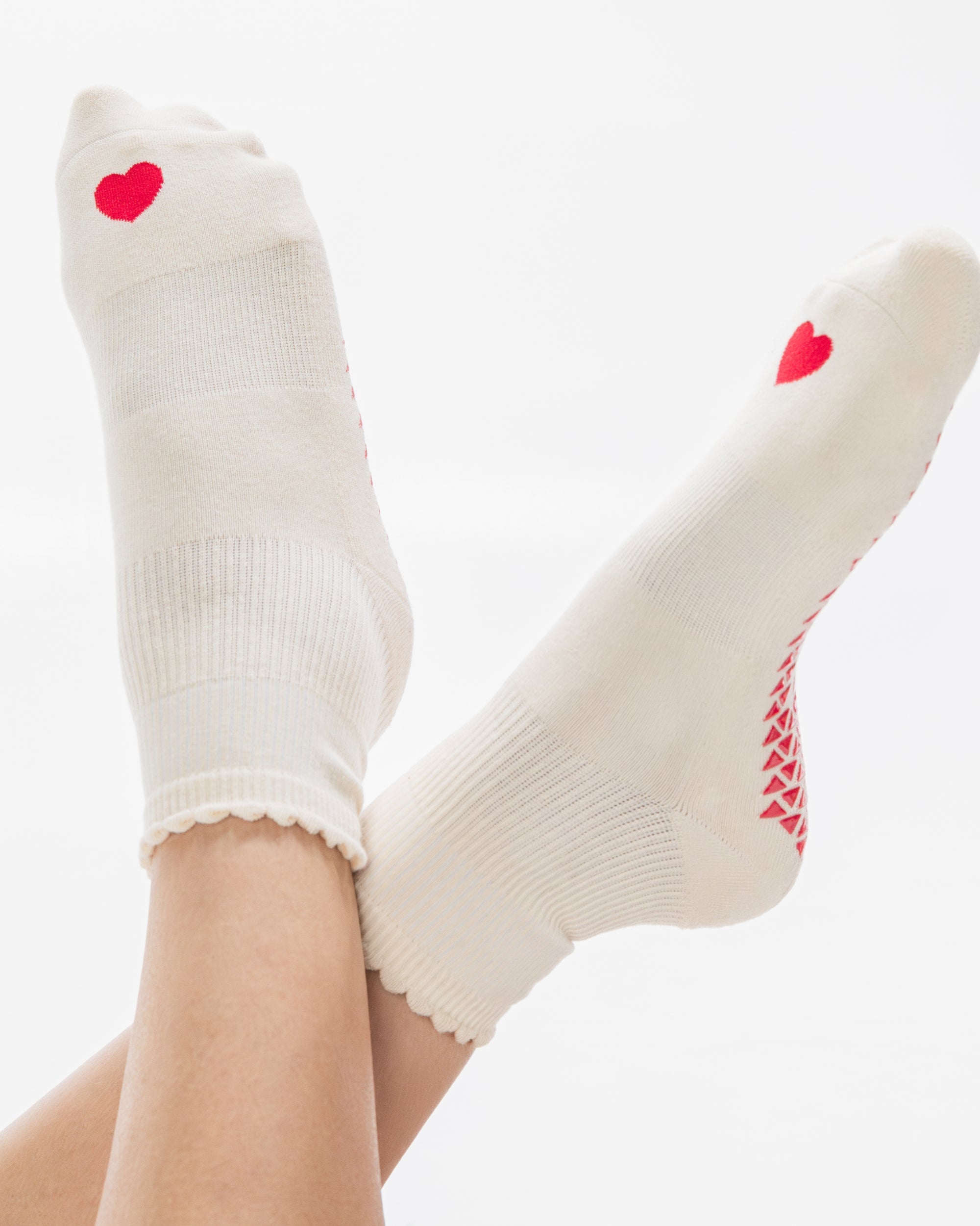 Women wearing a off white ankle grip sock with a red heart motif on the top made for Pilates, Barre, Yoga, and beyond. 